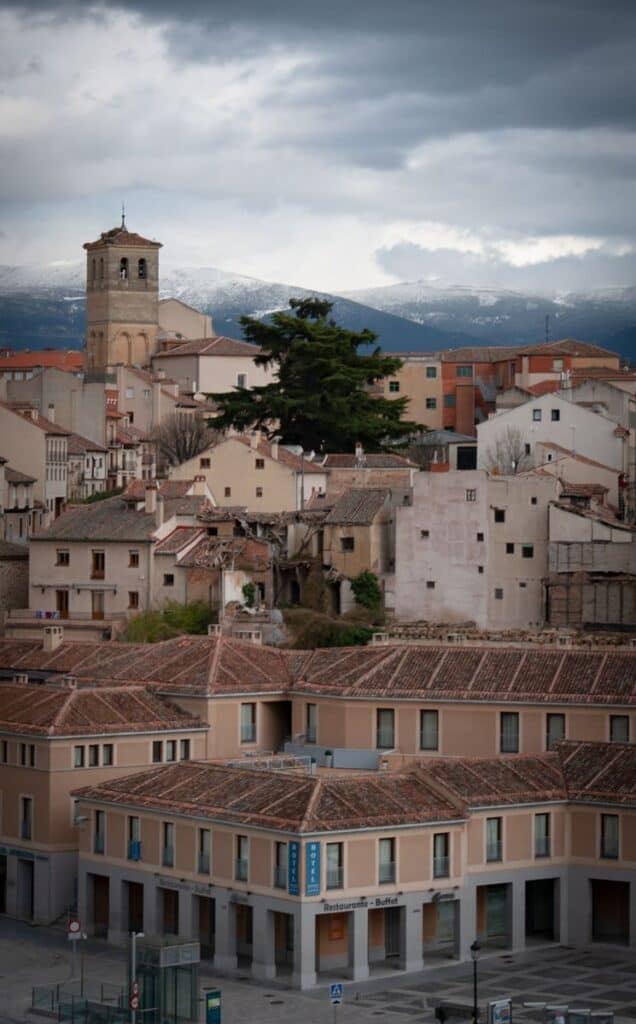 Explore Segovia's charming architecture with a backdrop of snow-capped mountains under overcast skies.